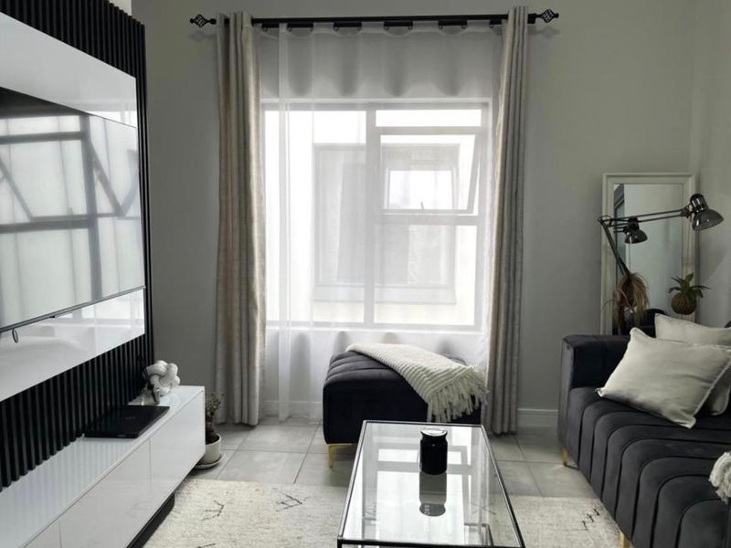 A modern living room featuring contemporary slatted wall paneling, neutral tiled flooring, and a large window with elegant curtain treatments.
