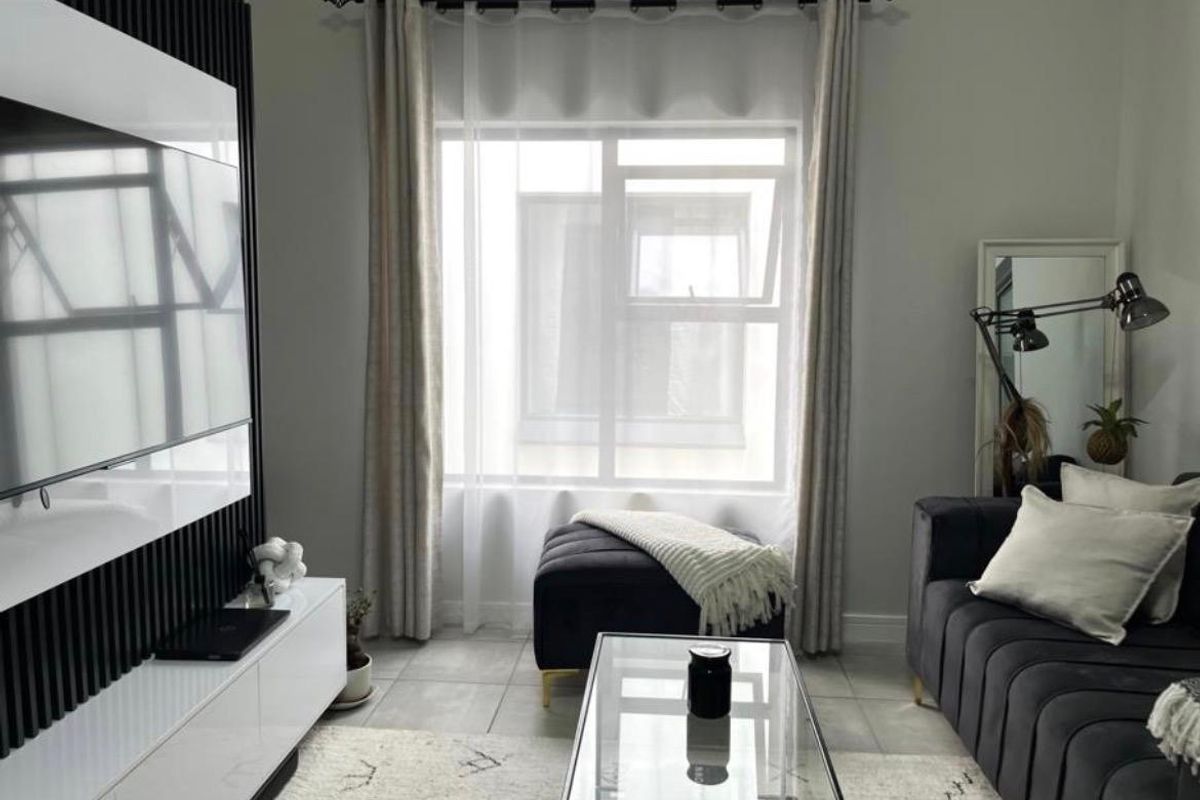 A modern living room featuring contemporary slatted wall paneling, neutral tiled flooring, and a large window with elegant curtain treatments.