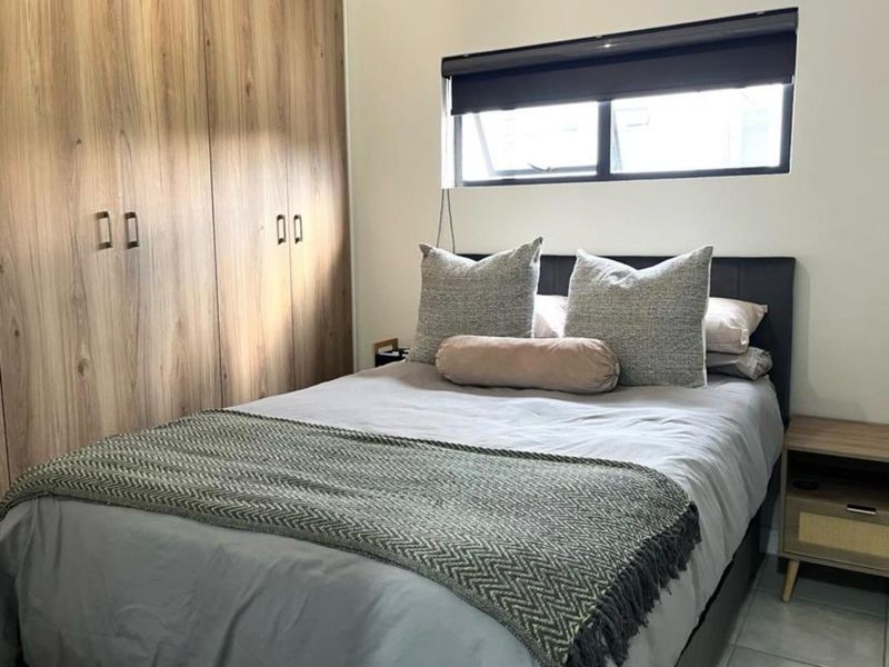 A well-maintained bedroom featuring modern wood-finish built-in cupboards and a functional roller blind.