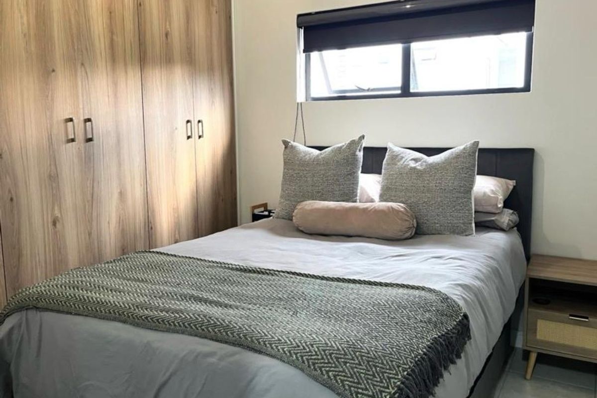 A well-maintained bedroom featuring modern wood-finish built-in cupboards and a functional roller blind.
