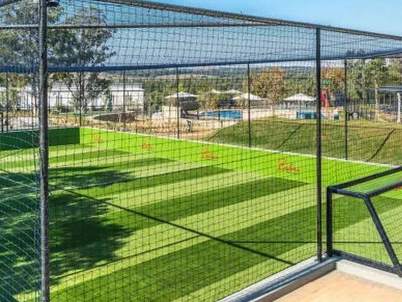 A well-maintained outdoor sports facility featuring artificial turf, enclosed by high perimeter netting and equipped with floodlights.