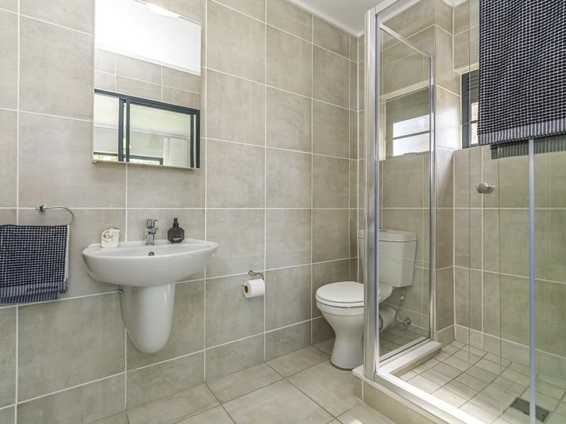 A clean, modern bathroom featuring neutral ceramic wall and floor tiles, a pedestal washbasin, and a glass-enclosed shower.