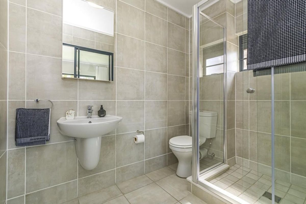 A clean, modern bathroom featuring neutral ceramic wall and floor tiles, a pedestal washbasin, and a glass-enclosed shower.