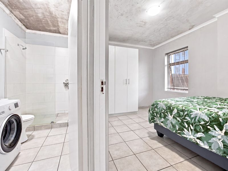 Bedroom featuring tiled flooring and a built-in wardrobe, with an adjacent en-suite bathroom containing a shower and toilet. Ceiling requires maintenance.