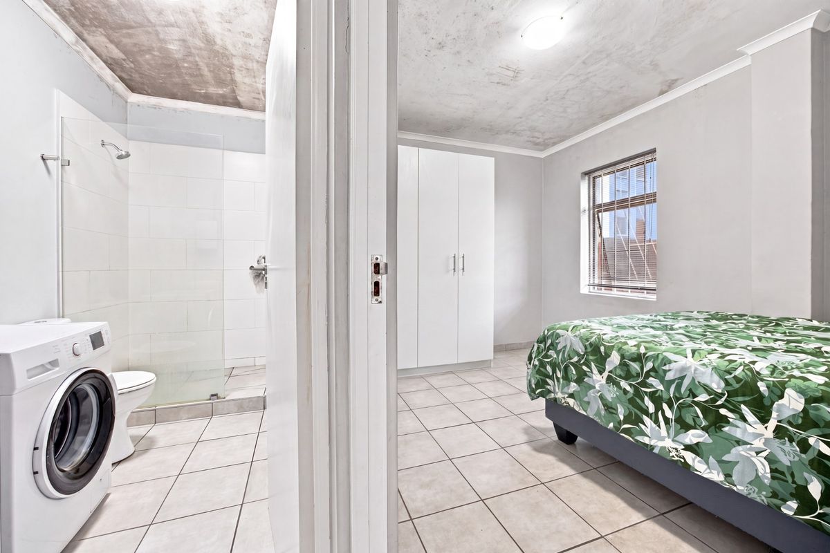 Bedroom featuring tiled flooring and a built-in wardrobe, with an adjacent en-suite bathroom containing a shower and toilet. Ceiling requires maintenance.