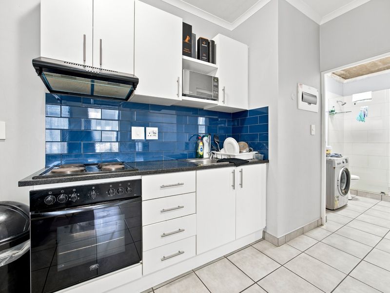 Compact kitchen featuring white cabinetry, a blue subway tile backsplash, built-in oven, hob, and extractor fan, with an adjacent laundry area.