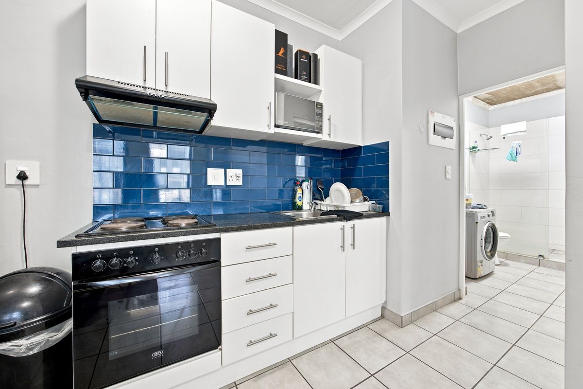 Compact kitchen featuring white cabinetry, a blue subway tile backsplash, built-in oven, hob, and extractor fan, with an adjacent laundry area.