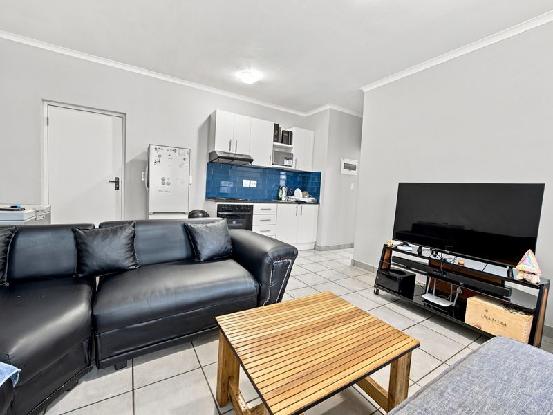 Open-plan living area featuring a compact kitchen with white cabinetry, blue tiled backsplash, and tiled flooring throughout the combined space.