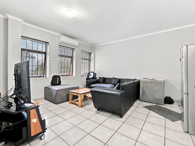 Open-plan living area featuring tiled flooring, split-system air conditioning, and large windows with security bars, offering a functional and versatile space.