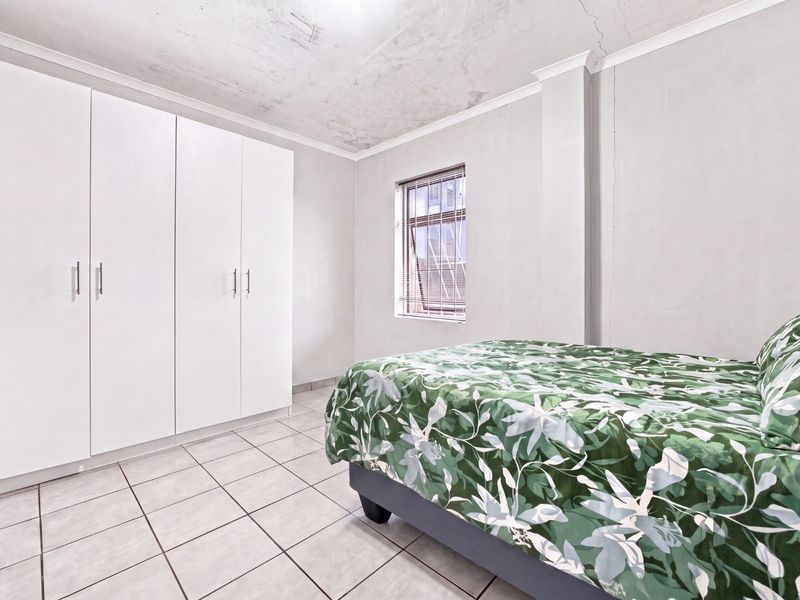 A bedroom featuring tiled flooring, a built-in wardrobe, and visible cracks on the ceiling and walls requiring maintenance.