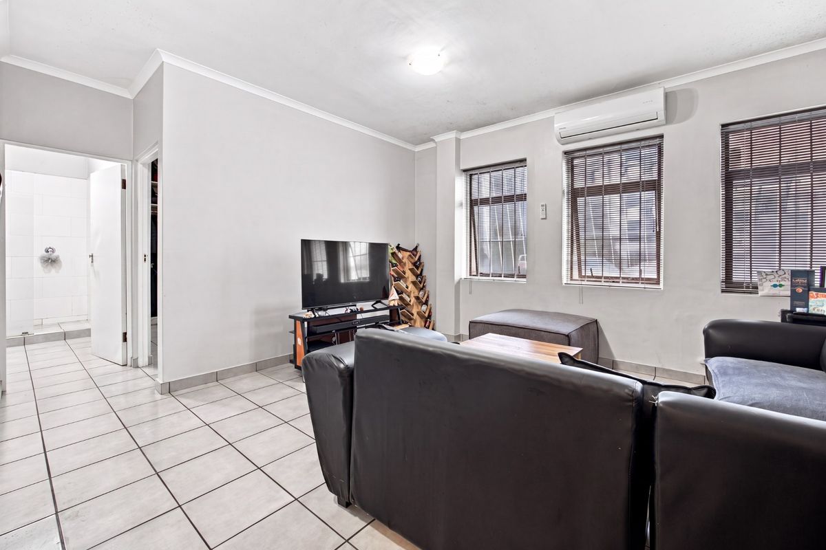 A living room featuring tiled flooring, a wall-mounted split-system air conditioner, and windows with fitted blinds, providing a functional and neutral living space.