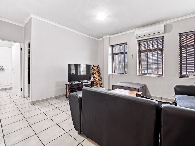 A living room featuring tiled flooring, a wall-mounted split-system air conditioner, and windows with fitted blinds, providing a functional and neutral living space.