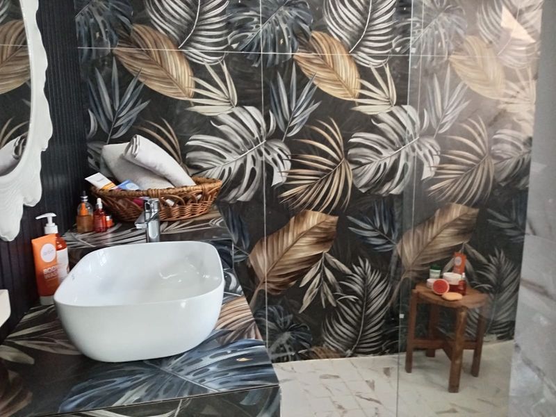 A modern bathroom featuring a vessel sink, chrome tapware, and striking botanical-patterned wall tiles with a glass shower screen.
