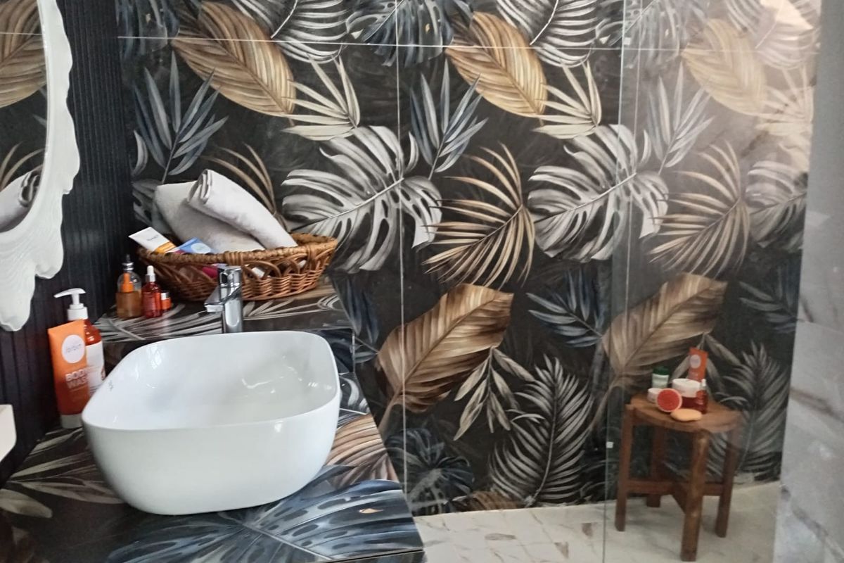 A modern bathroom featuring a vessel sink, chrome tapware, and striking botanical-patterned wall tiles with a glass shower screen.