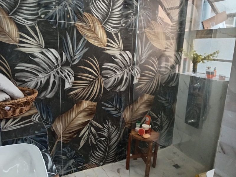A modern bathroom featuring a walk-in shower with striking botanical patterned wall tiles and a glass partition.