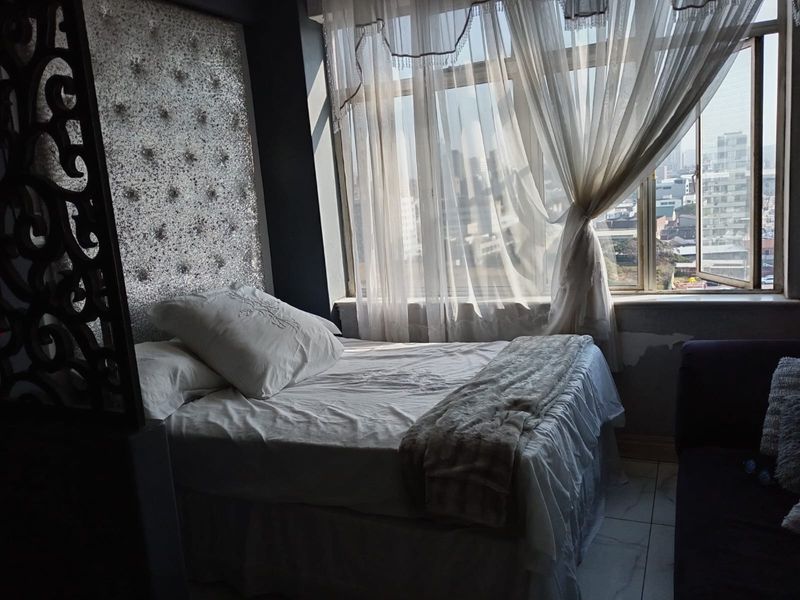 A bedroom featuring a large window with city views, tiled flooring, and a decorative wall panel behind the bed area.