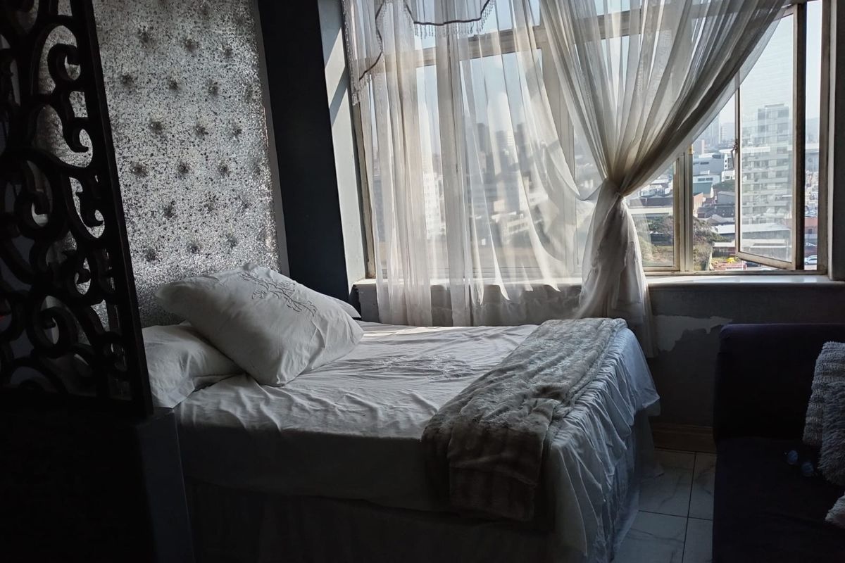 A bedroom featuring a large window with city views, tiled flooring, and a decorative wall panel behind the bed area.