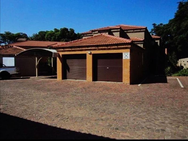 Exterior view of the property featuring a double garage with roller shutter doors, a paved driveway, and an attached carport.