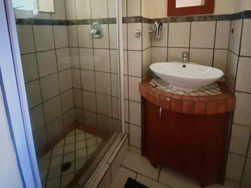 Compact bathroom featuring a corner vanity with a vessel sink and a separate tiled shower enclosure.