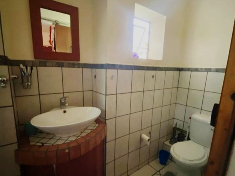 A compact bathroom featuring a vessel sink on a corner vanity cabinet, a standard toilet, and tiled wall and floor finishes.