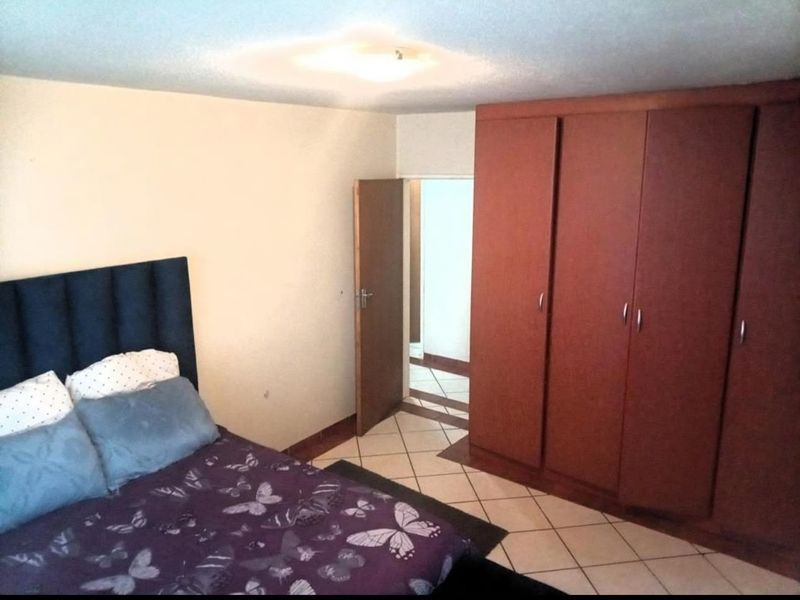 A bedroom featuring tiled flooring, a large built-in wooden wardrobe, and direct access to an adjacent hallway.