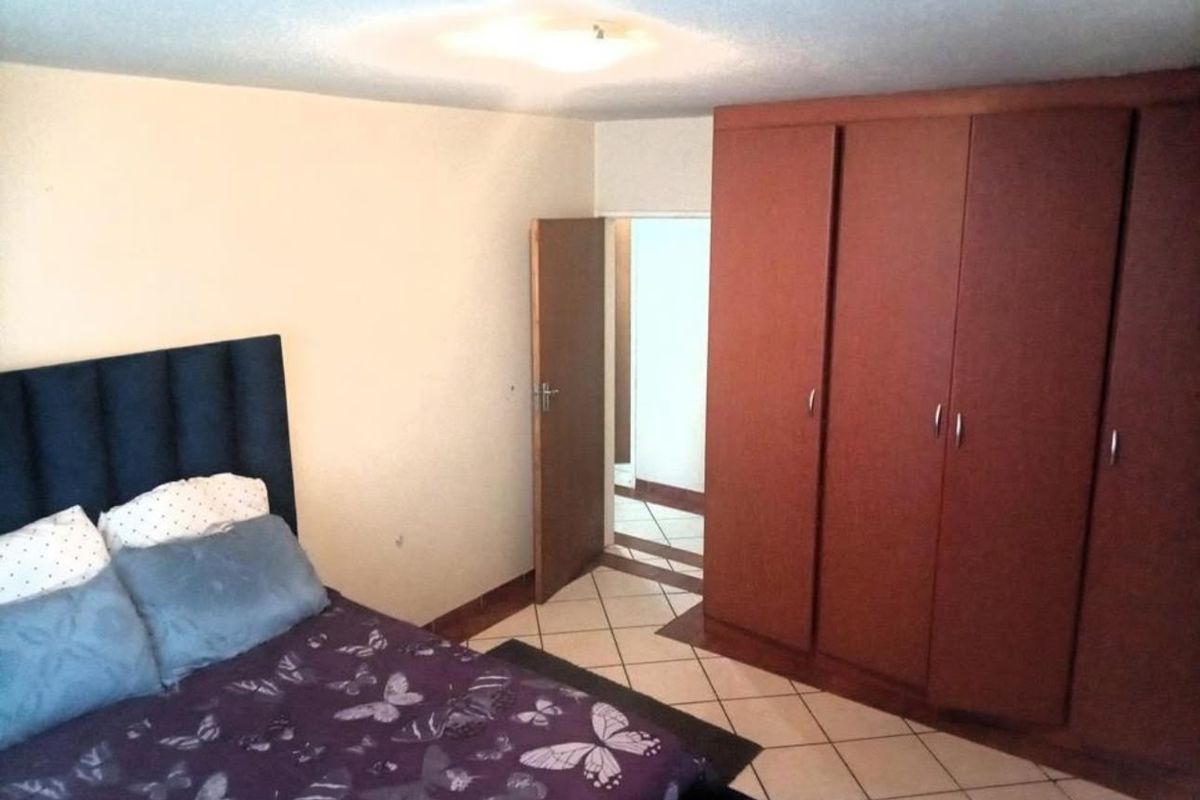A bedroom featuring tiled flooring, a large built-in wooden wardrobe, and direct access to an adjacent hallway.