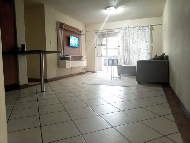 Open-plan living area featuring tiled flooring, a built-in media console, and a sliding glass door providing access to the exterior.