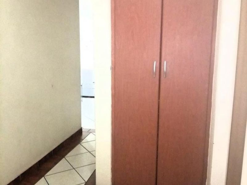 A narrow hallway featuring built-in wooden cupboards and tiled flooring, providing functional storage space within the apartment.