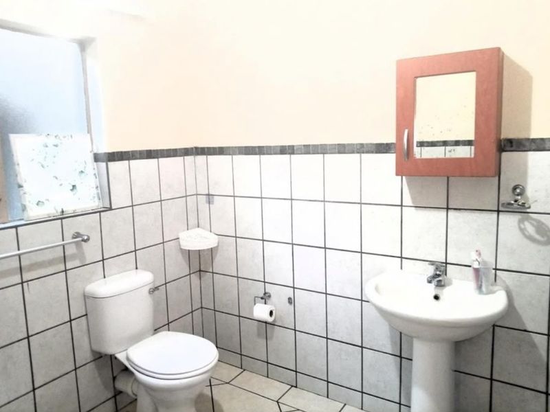 A functional bathroom featuring a pedestal basin, toilet, and wall-mounted medicine cabinet with tiled finishes throughout.