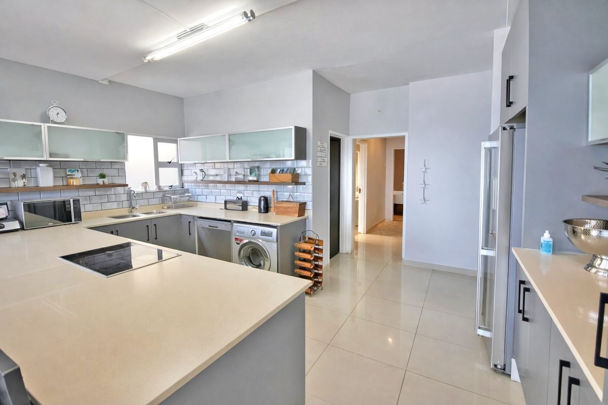 Modern kitchen featuring stone countertops, subway tile backsplash, ample built-in cabinetry, and integrated hob, with tiled flooring throughout.