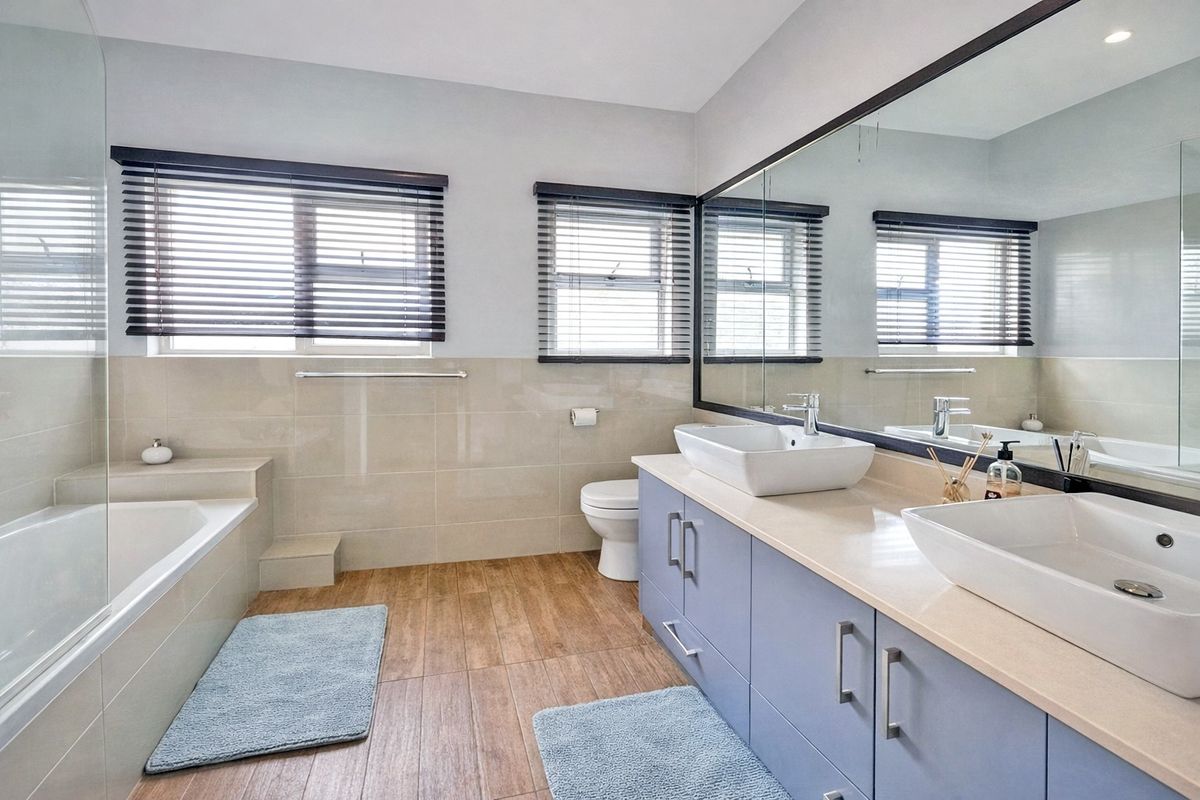 Modern bathroom featuring a double vanity with vessel sinks, a built-in bathtub with a glass screen, and large wall-to-wall mirror.