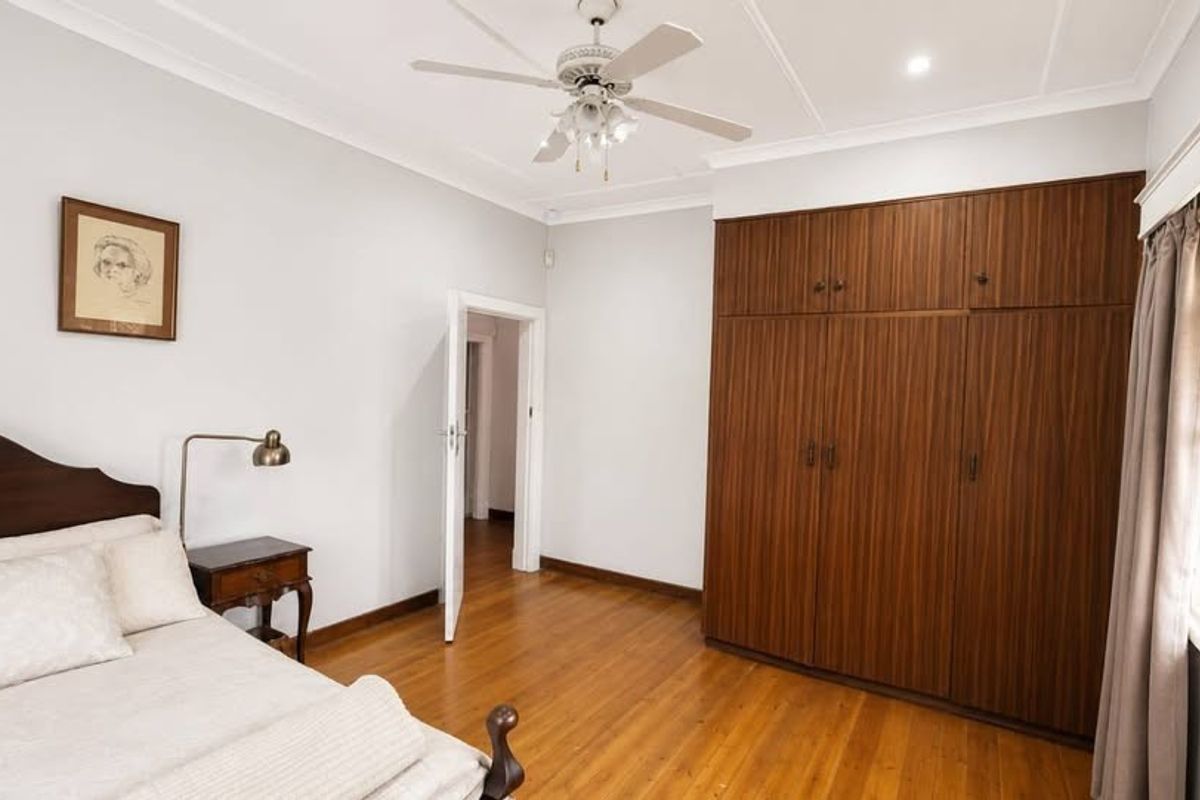 A well-maintained bedroom featuring polished hardwood flooring, a large built-in wooden wardrobe, and a ceiling fan.