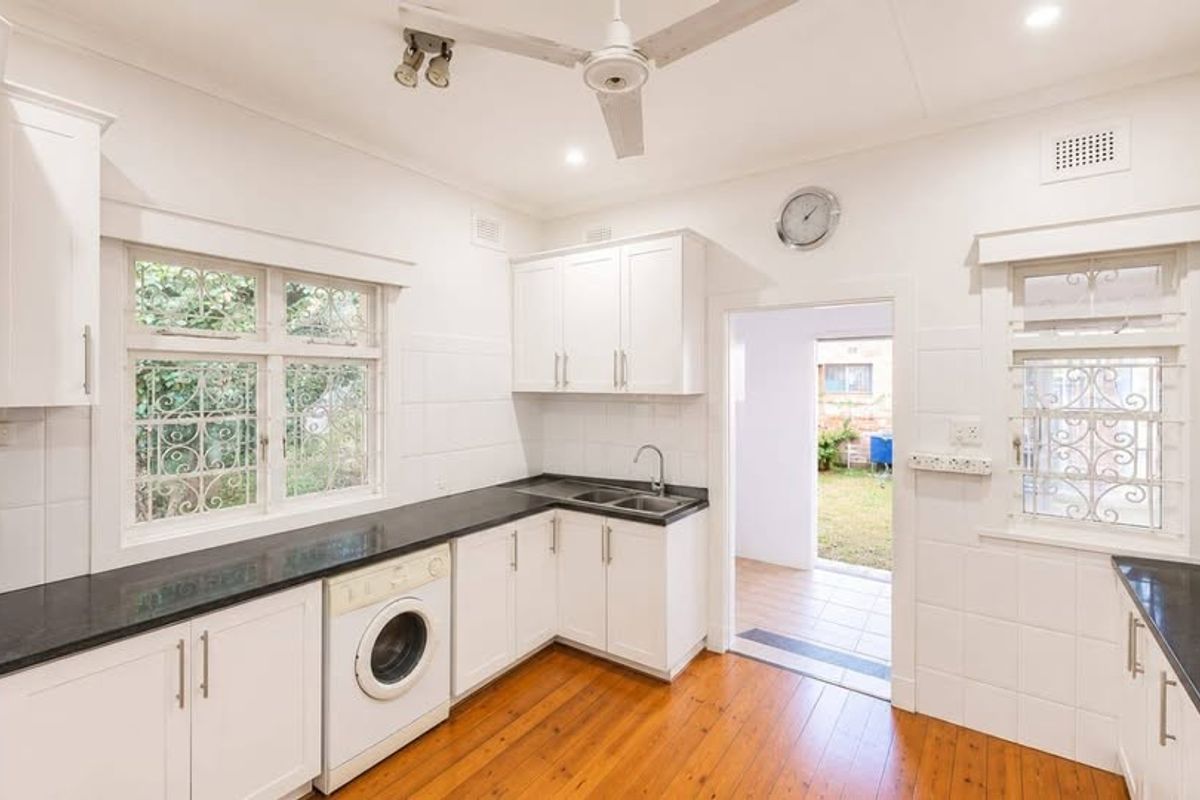 A bright, functional kitchen featuring white cabinetry, contrasting black countertops, timber flooring, and direct access to the rear outdoor area.