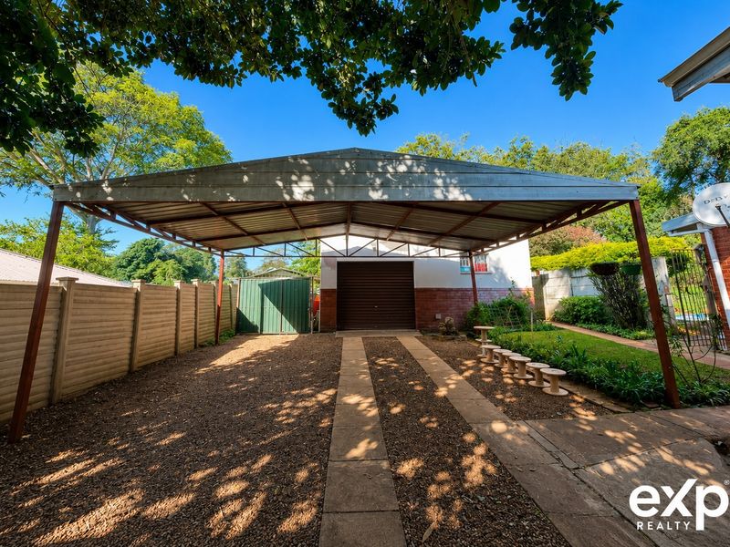 A spacious outdoor carport with a metal roof structure, concrete driveway tracks, and a secure roll-up garage door entrance.