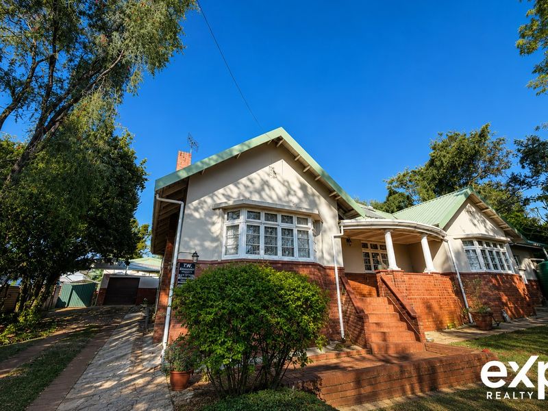 A charming single-story brick house featuring a metal roof, bay windows, a covered front porch with brick stairs, and a detached garage.
