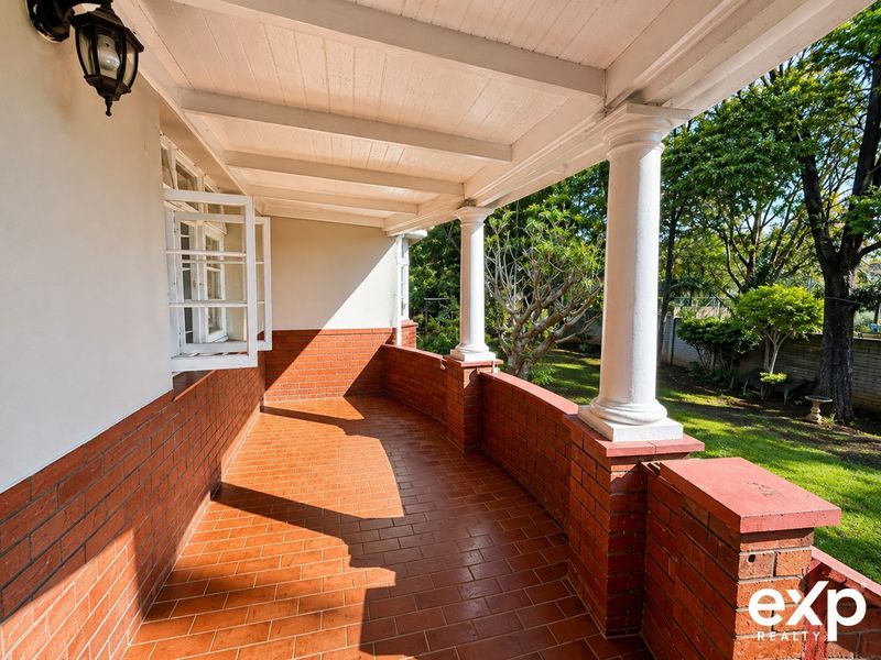 A covered patio featuring classic columns, brick flooring, and a brick balustrade, overlooking the garden area.