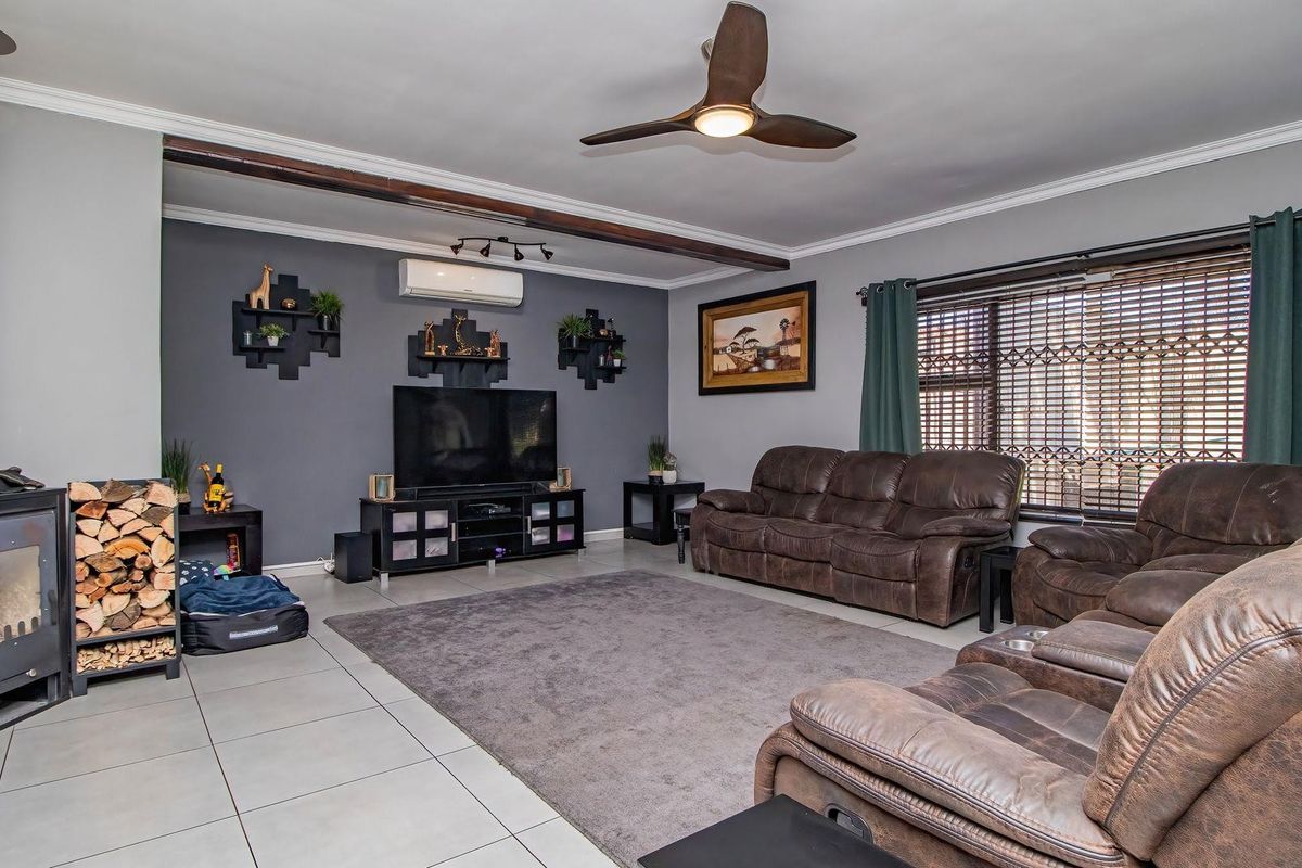 Spacious living room featuring a wood-burning fireplace, ceiling fan, split-system air conditioning, and neutral tiled flooring with crown molding details.