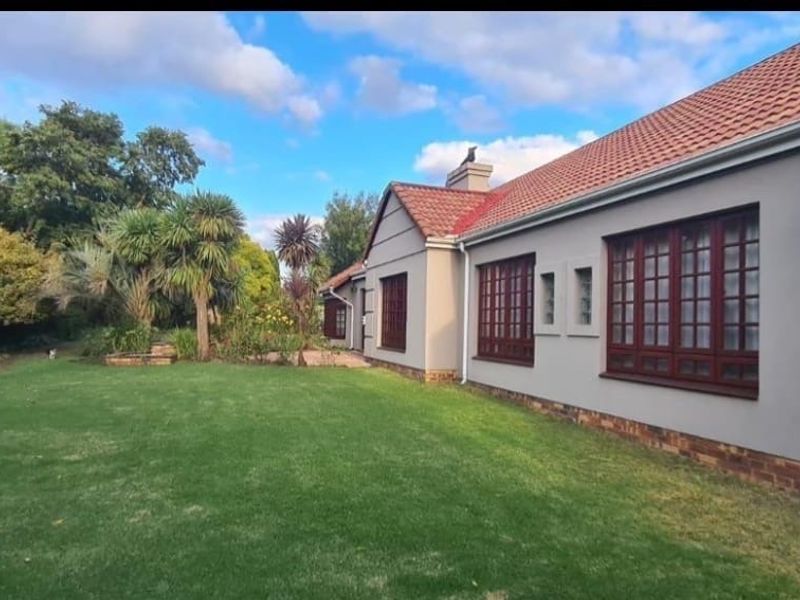 A view of the rear elevation of the house featuring a well-maintained lawn, mature garden, and traditional timber-framed windows.