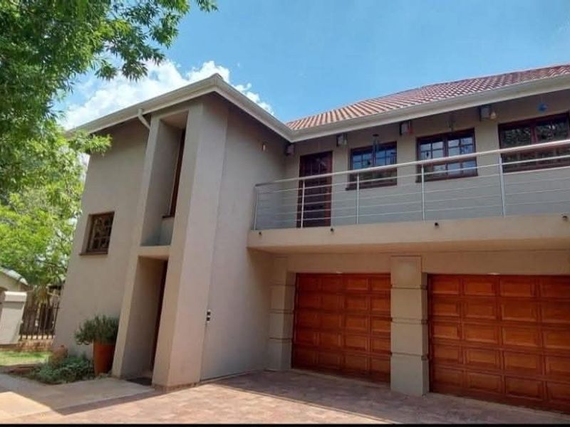 Front elevation of a double-story house featuring a double garage with wooden doors and an upper-level balcony with a stainless steel balustrade.