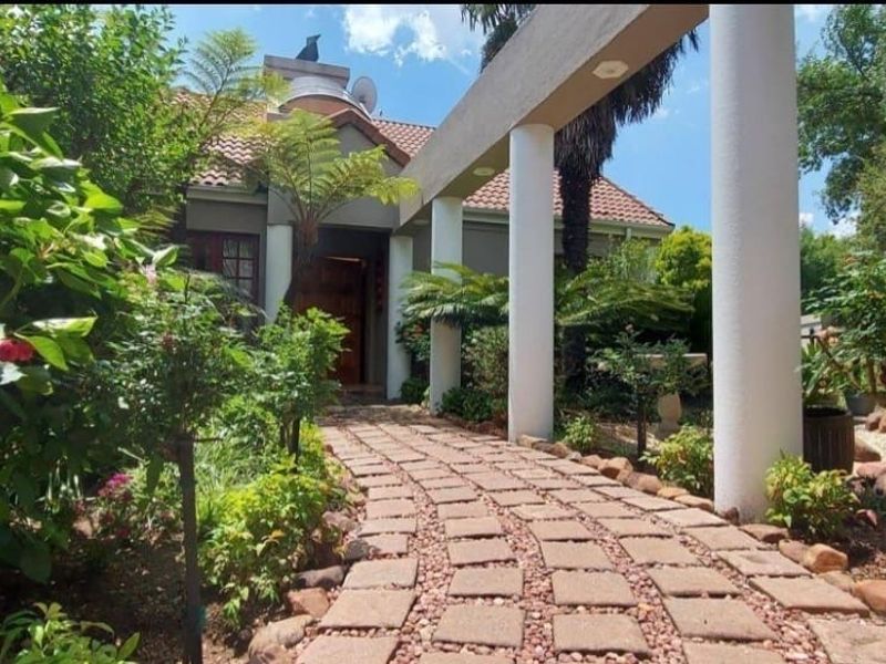 A welcoming front entrance featuring a paved walkway leading to the home, framed by structural columns and a well-maintained garden.