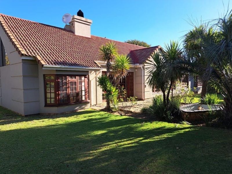 Rear view of the house featuring a terracotta tiled roof, chimney, bay window, and a stone paved patio overlooking a well-maintained garden.