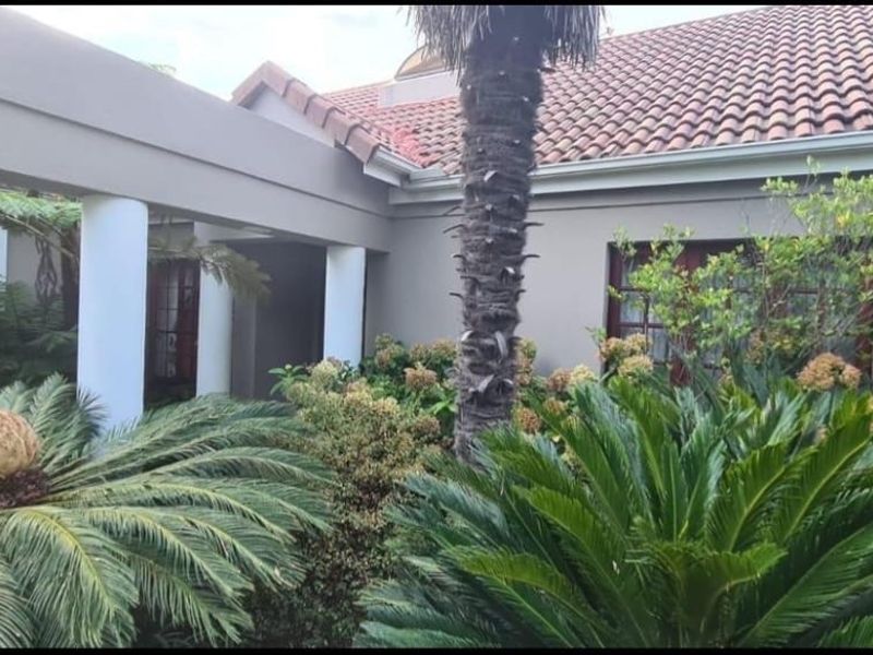 Front facade of the house featuring a covered entrance, structural columns, and a well-established landscaped garden.