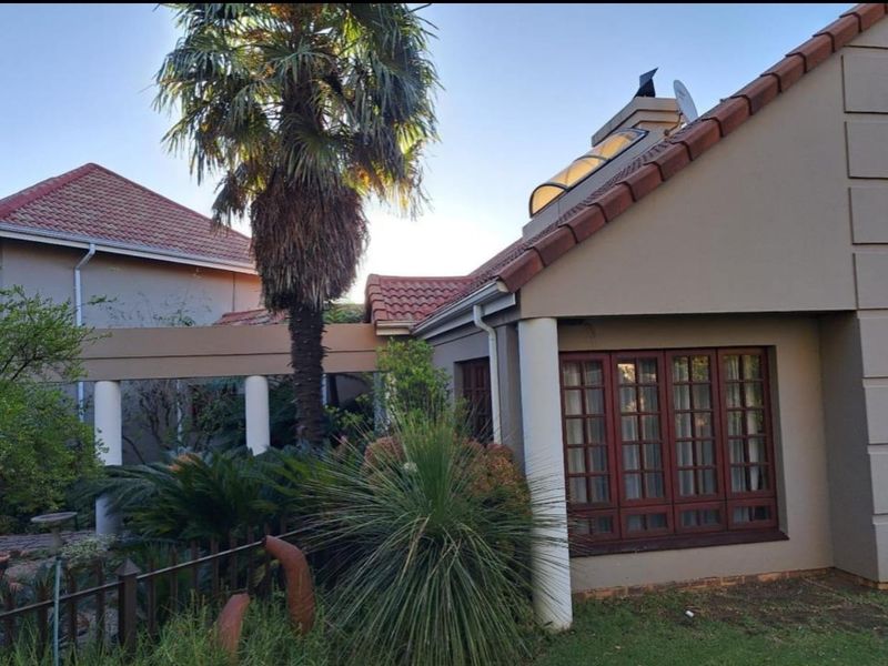 Rear exterior view of the house featuring a tiled roof, skylight, and a covered walkway with columns, set within a landscaped garden area.