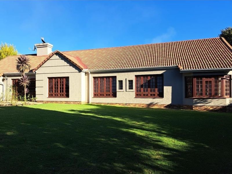 Rear view of the house featuring a well-maintained lawn, terracotta tiled roof, and classic timber-framed windows set against a clear blue sky.