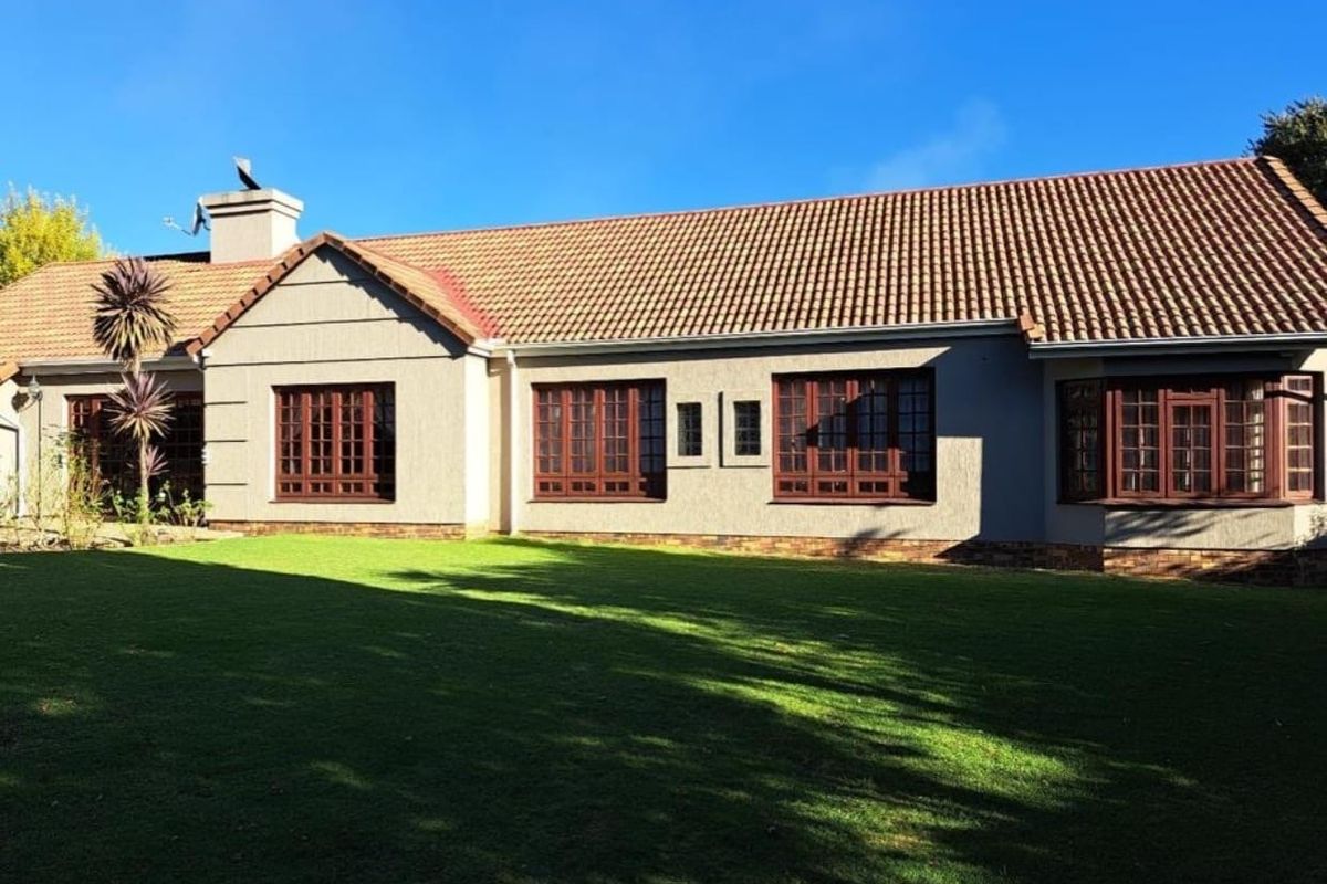 Rear view of the house featuring a well-maintained lawn, terracotta tiled roof, and classic timber-framed windows set against a clear blue sky.
