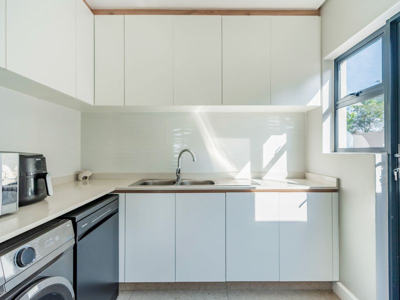 A modern, well-maintained scullery featuring clean white cabinetry, stone countertops, a stainless steel sink, and direct access to the exterior.
