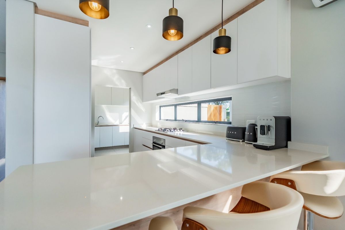 Modern kitchen featuring sleek handleless cabinetry, quartz countertops, integrated appliances, and a breakfast bar, with an adjacent scullery area.