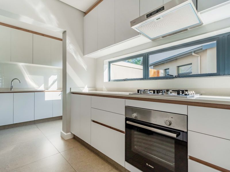 Modern kitchen featuring sleek white cabinetry, stone countertops, integrated gas cooktop, built-in oven, and a separate scullery area with additional sink and storage.