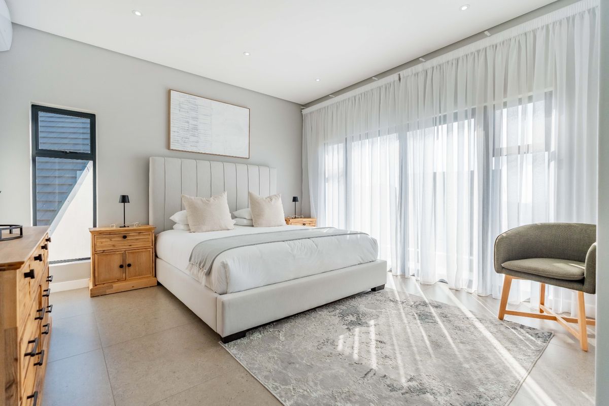 A bright and modern bedroom featuring neutral tones, tiled flooring, recessed lighting, and large sliding glass doors that provide ample natural light.