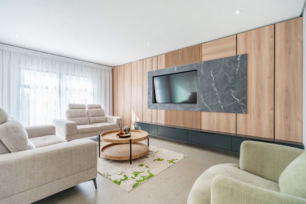 Modern living room featuring a sophisticated wood-paneled feature wall with integrated media unit, recessed lighting, and large windows with sheer curtains.